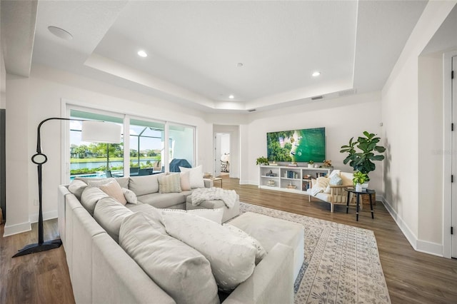 living room featuring baseboards, a tray ceiling, recessed lighting, and wood finished floors