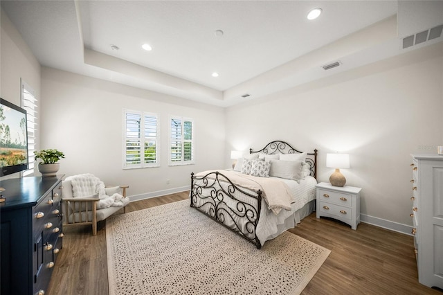 bedroom with dark wood-style flooring, baseboards, visible vents, and a raised ceiling