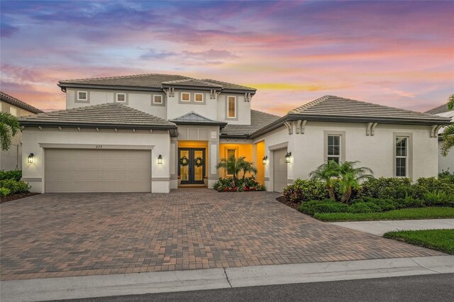 prairie-style home featuring french doors, decorative driveway, and a garage