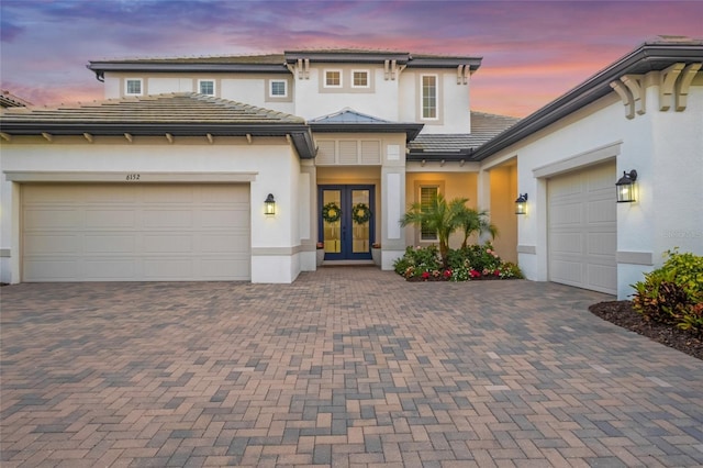 view of front of property featuring stucco siding, decorative driveway, french doors, and a garage