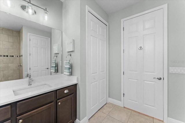 full bath featuring vanity, a closet, baseboards, tile patterned floors, and a tile shower