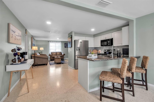 kitchen with visible vents, a peninsula, baseboards, dark stone countertops, and appliances with stainless steel finishes
