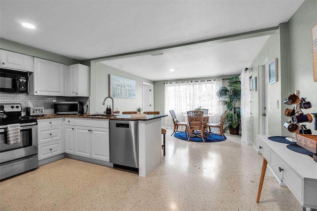 kitchen featuring stainless steel appliances, white cabinetry, a sink, and a peninsula