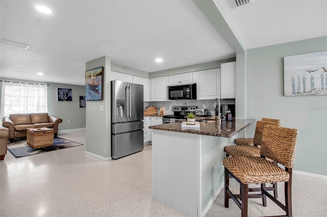 kitchen featuring a sink, white cabinets, dark stone countertops, a peninsula, and stainless steel appliances