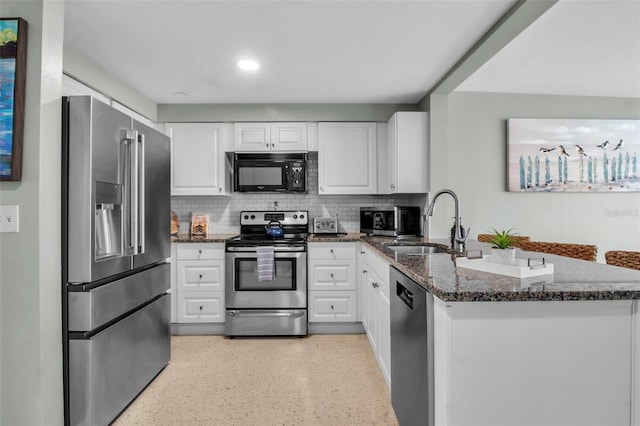 kitchen featuring a peninsula, white cabinetry, a sink, dark stone countertops, and appliances with stainless steel finishes