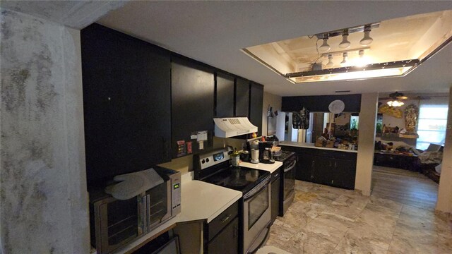 kitchen featuring stainless steel range with electric stovetop, white microwave, under cabinet range hood, a tray ceiling, and dark cabinets
