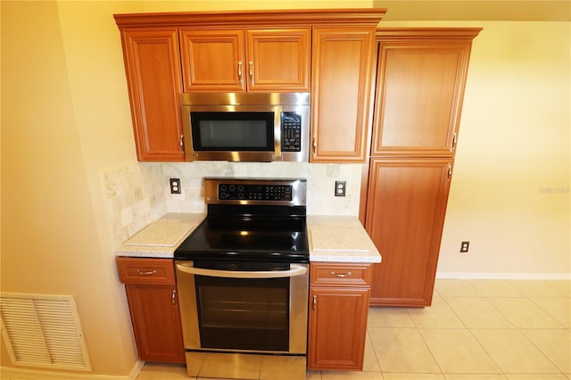 2521 Tamarind Dr, Edgewater, FL 32141 - kitchen featuring light tile patterned flooring, brown cabinetry, visible vents, backsplash, and appliances with stainless steel finishes