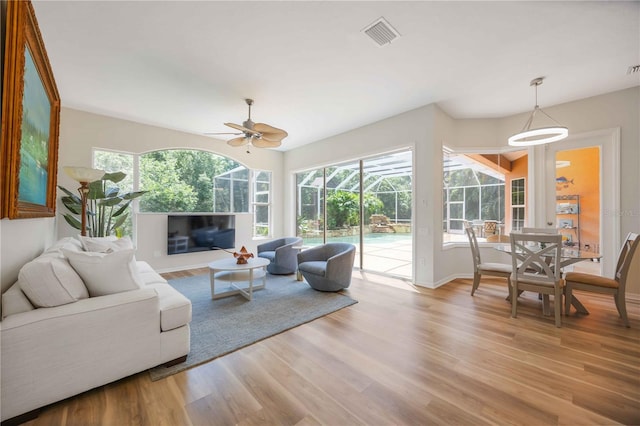 living room featuring ceiling fan, light wood-style flooring, a sunroom, and baseboards