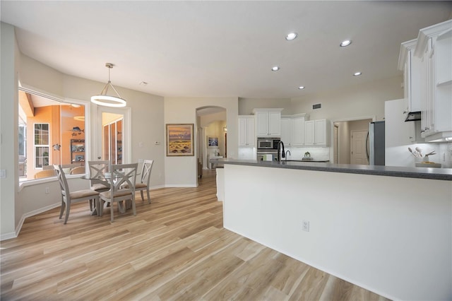 kitchen featuring arched walkways, white cabinets, dark countertops, light wood-type flooring, and baseboards