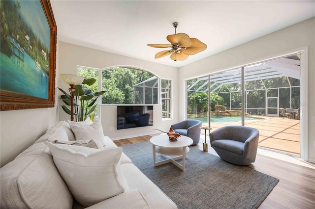 living area featuring a sunroom, wood finished floors, ceiling fan, and plenty of natural light
