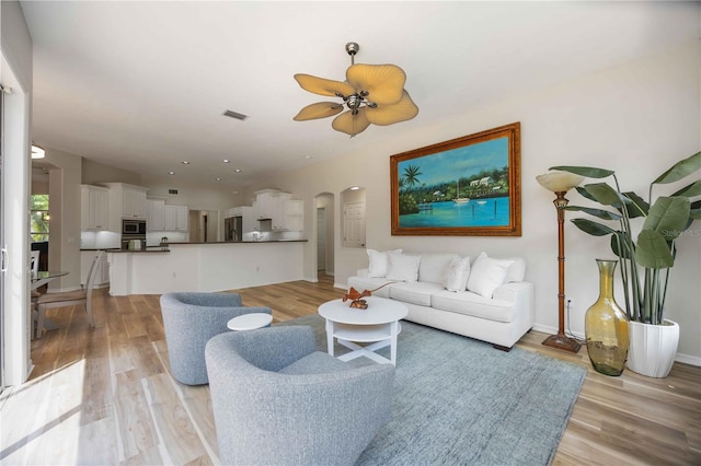 living area with arched walkways, ceiling fan, light wood-type flooring, baseboards, and recessed lighting