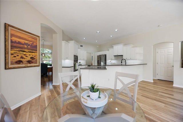 dining area featuring light wood-type flooring, baseboards, arched walkways, and recessed lighting
