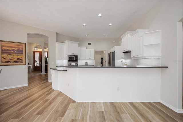 kitchen with arched walkways, open shelves, appliances with stainless steel finishes, dark countertops, and white cabinets
