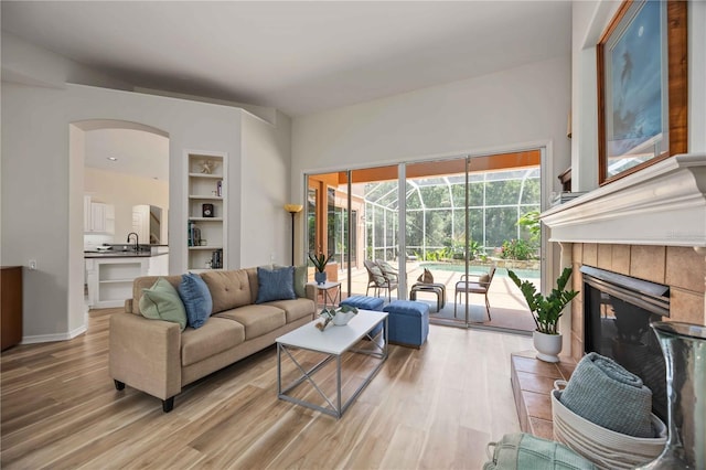 living area with light wood-type flooring, arched walkways, a sunroom, built in features, and a fireplace