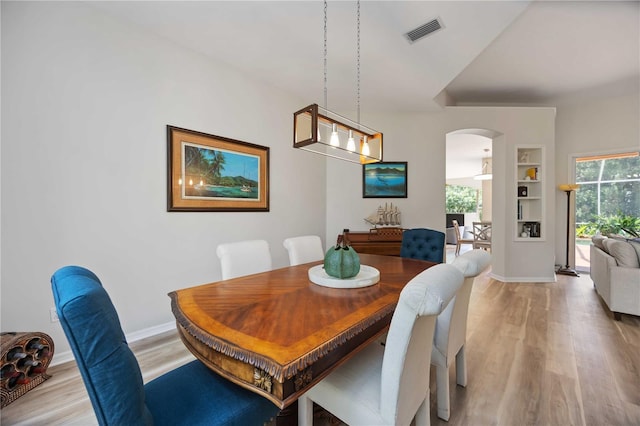 dining area with arched walkways, light wood-style flooring, and plenty of natural light
