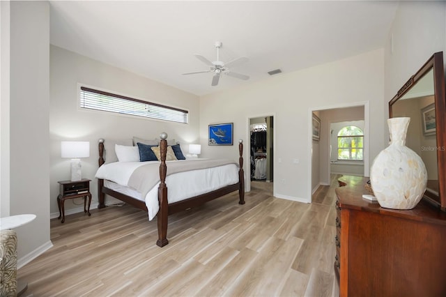 bedroom featuring a spacious closet, light wood-style flooring, baseboards, ceiling fan, and a closet