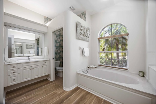 bathroom with a bath, vanity, toilet, and wood finished floors