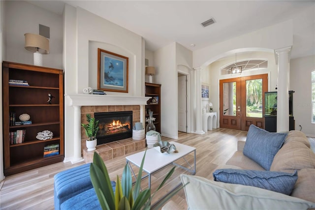 living room with ornate columns, light wood-type flooring, a tile fireplace, and built in shelves