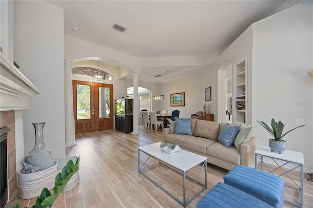living area featuring ornate columns, arched walkways, light wood-style flooring, built in features, and a tile fireplace