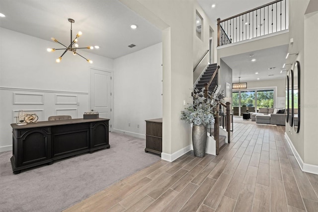 foyer entrance with an inviting chandelier, visible vents, a towering ceiling, stairway, and light wood finished floors