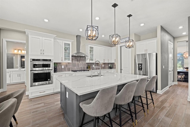 kitchen with a sink, wall chimney range hood, stainless steel appliances, and a chandelier