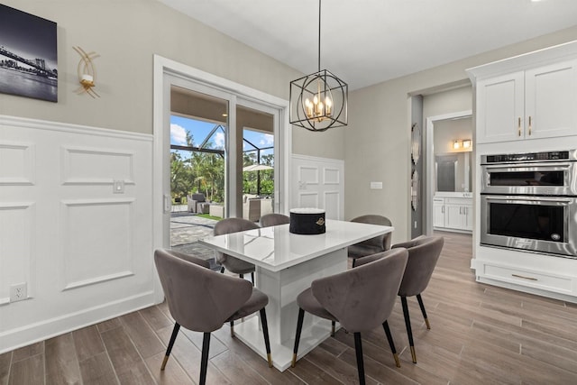dining space featuring wainscoting, a decorative wall, wood finished floors, and a notable chandelier