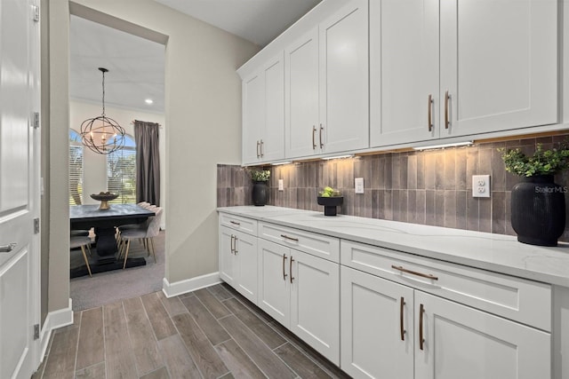 bar with baseboards, dark wood-style floors, backsplash, a notable chandelier, and decorative light fixtures