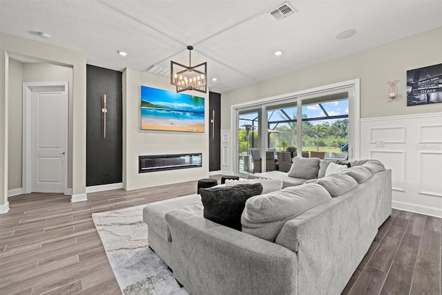 living area featuring an inviting chandelier, a fireplace, wood finished floors, and visible vents