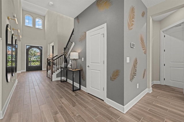 entrance foyer with baseboards, a high ceiling, stairway, and light wood-style floors