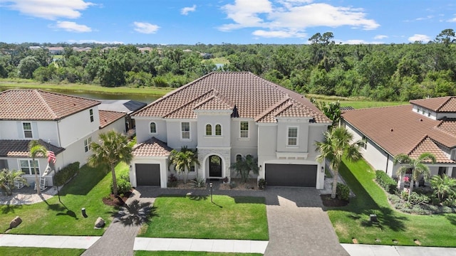 mediterranean / spanish-style home with driveway, a tile roof, a garage, a front lawn, and stucco siding