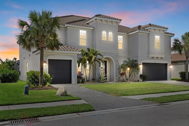 mediterranean / spanish home with a lawn, an attached garage, driveway, and a tile roof