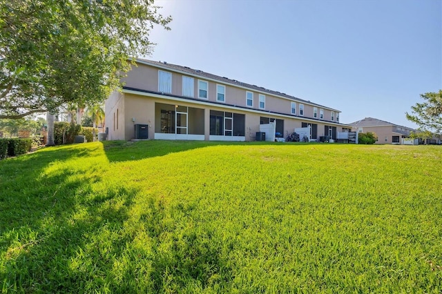 rear view of house with central air condition unit, a lawn, and stucco siding