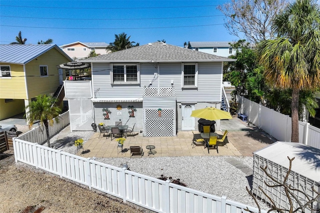 rear view of house featuring a patio, a fenced backyard, roof with shingles, and outdoor dining space