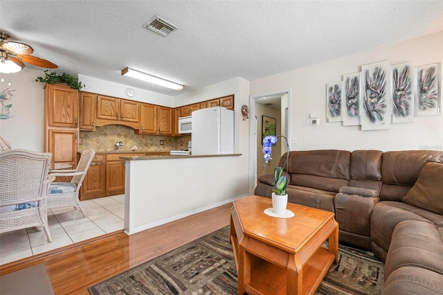 living area with light wood-style floors, a ceiling fan, a textured ceiling, and visible vents