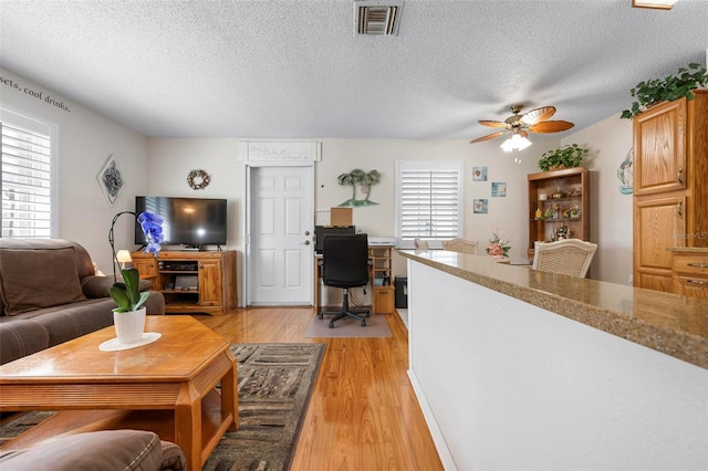 living room featuring a textured ceiling, ceiling fan, visible vents, and light wood-style floors