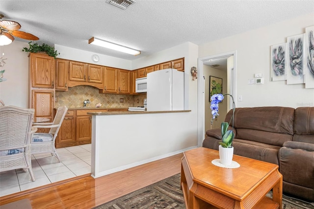 kitchen featuring decorative backsplash, visible vents, a peninsula, light wood-style floors, and white appliances
