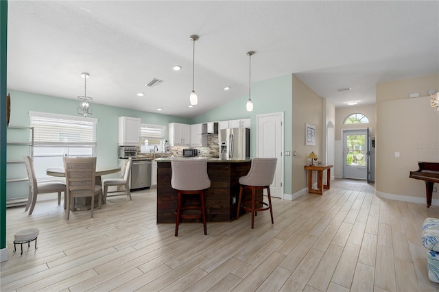 kitchen featuring wall chimney exhaust hood, stainless steel appliances, white cabinetry, visible vents, and lofted ceiling