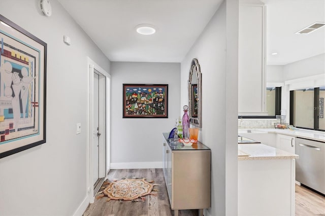 corridor with baseboards, light wood finished floors, and visible vents