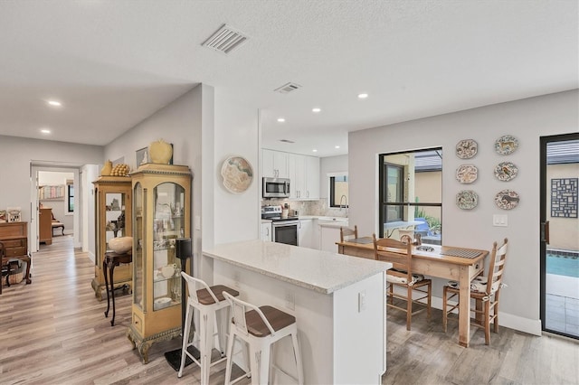 kitchen featuring visible vents, a peninsula, light wood-type flooring, white cabinetry, and appliances with stainless steel finishes