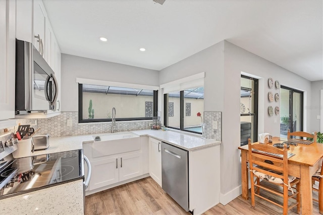 kitchen with a sink, white cabinets, light wood-style floors, and stainless steel appliances