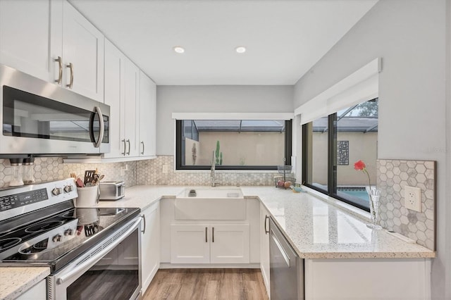 kitchen featuring backsplash, appliances with stainless steel finishes, a sink, white cabinets, and light wood finished floors