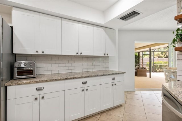 kitchen with white cabinets, stainless steel dishwasher, visible vents, decorative backsplash, and light stone counters