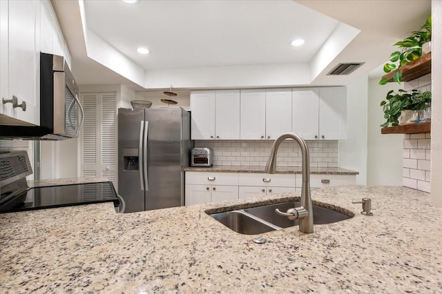 kitchen featuring a sink, stainless steel appliances, white cabinets, visible vents, and light stone counters