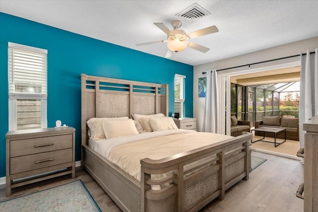 bedroom with a ceiling fan, a textured ceiling, visible vents, light wood-type flooring, and access to exterior