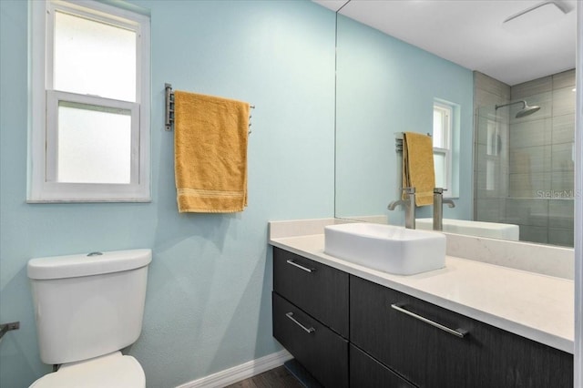 bathroom with toilet, a tile shower, vanity, and baseboards