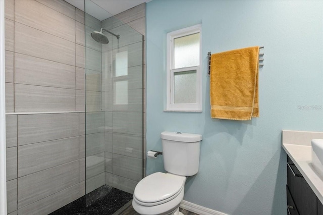 bathroom with toilet, baseboards, vanity, and tiled shower