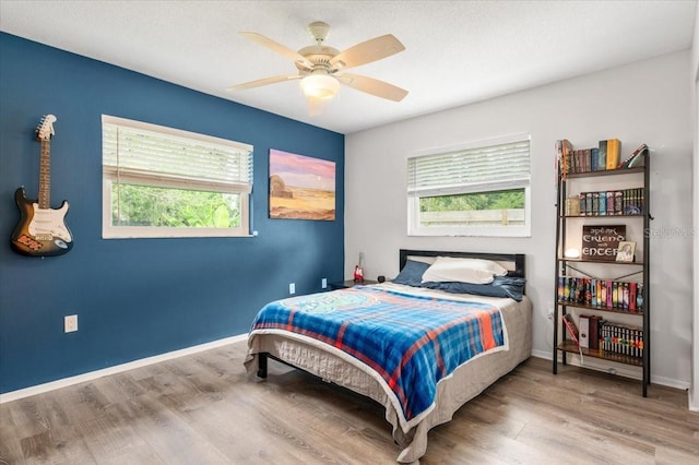 bedroom with multiple windows, a ceiling fan, wood finished floors, and baseboards