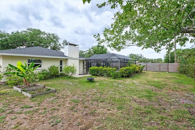 view of yard featuring an outdoor fire pit, a vegetable garden, a lanai, and fence