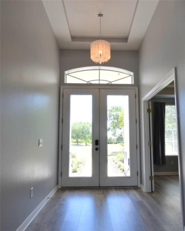 doorway featuring wood finished floors, baseboards, a chandelier, a tray ceiling, and french doors