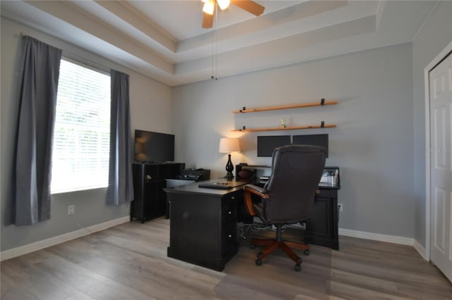 home office featuring light wood-type flooring, a ceiling fan, baseboards, and a tray ceiling